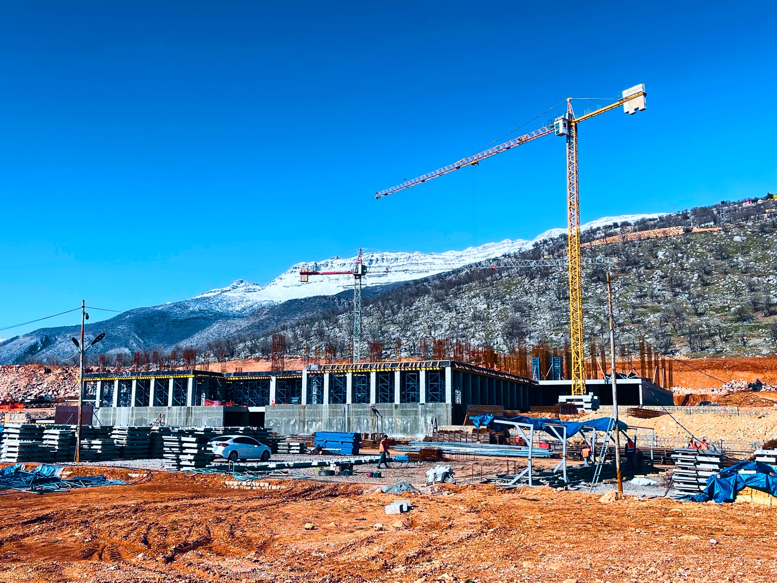 Formwork: concrete columns and slab shoring under a tower crane, snow-capped mountains behind the site