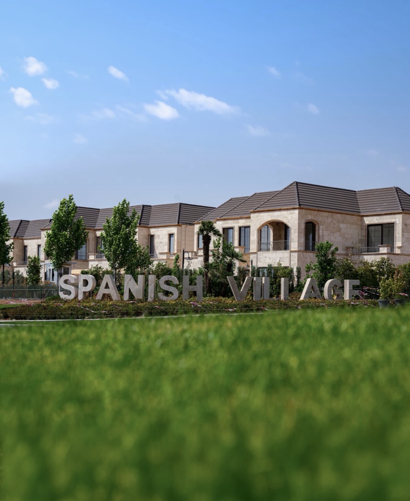 Spanish Village 2: stone-clad villas with tiled roofs and arched balconies behind the Spanish Village sign and a lawn